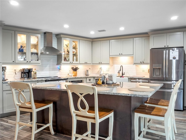 kitchen with wall chimney exhaust hood, a breakfast bar, stainless steel appliances, dark wood-type flooring, and a center island