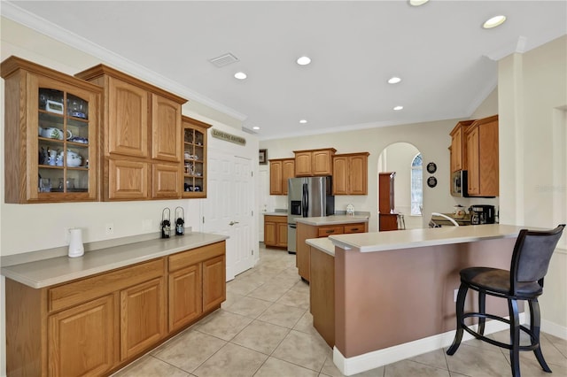 kitchen with light tile patterned floors, ornamental molding, a kitchen bar, kitchen peninsula, and stainless steel appliances