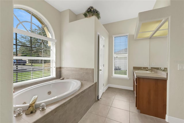 bathroom with tile patterned flooring, vanity, tiled bath, and a healthy amount of sunlight