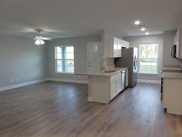 kitchen with light stone countertops, appliances with stainless steel finishes, sink, hardwood / wood-style flooring, and white cabinets