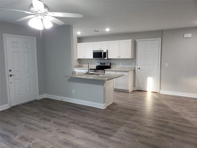 kitchen with light stone countertops, white cabinetry, stainless steel appliances, and wood-type flooring