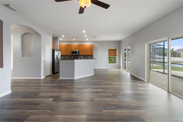 kitchen featuring a kitchen island with sink, dark hardwood / wood-style floors, ceiling fan, decorative backsplash, and appliances with stainless steel finishes