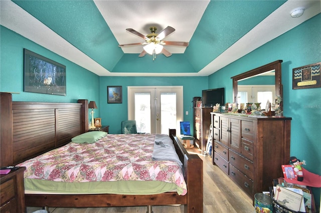 bedroom featuring a raised ceiling, ceiling fan, french doors, and light wood-type flooring