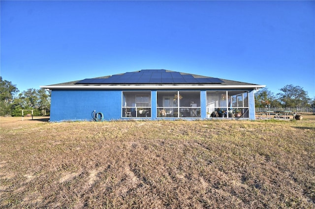 back of property with a sunroom, solar panels, and a yard