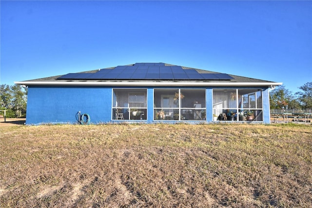 rear view of property featuring a lawn, a sunroom, and solar panels