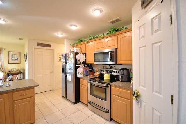 kitchen with light brown cabinetry, light tile patterned floors, stainless steel appliances, and a textured ceiling