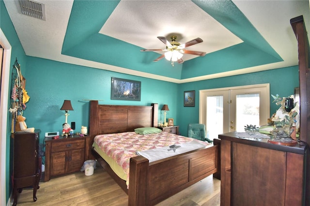 bedroom featuring ceiling fan, light hardwood / wood-style flooring, a tray ceiling, and french doors