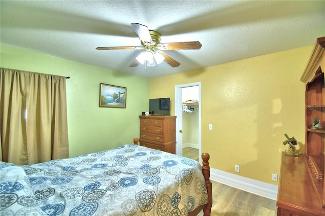 bedroom with a spacious closet, ceiling fan, a textured ceiling, a closet, and hardwood / wood-style flooring