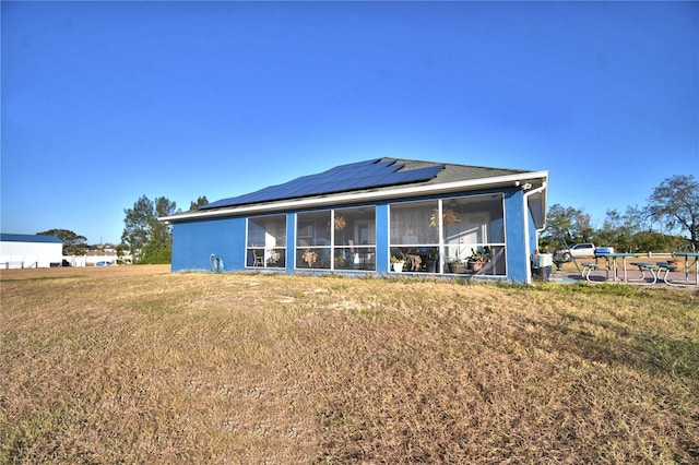 back of property featuring a lawn, a sunroom, and solar panels