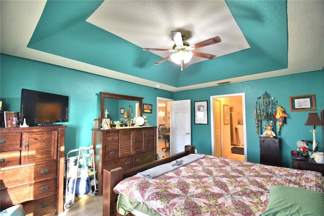 bedroom featuring a tray ceiling, connected bathroom, ceiling fan, and hardwood / wood-style floors