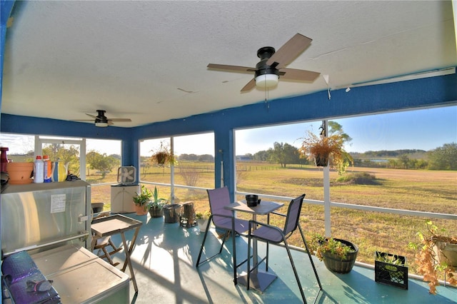 sunroom / solarium featuring ceiling fan and a rural view