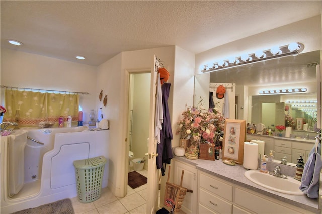 bathroom with a tub to relax in, tile patterned floors, a textured ceiling, vanity, and toilet