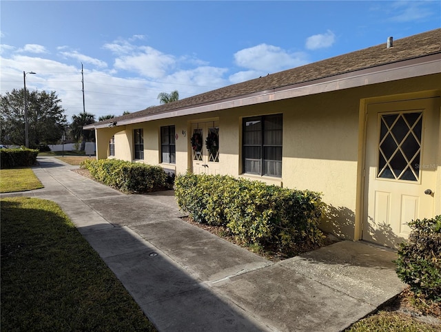 exterior space featuring a shingled roof and stucco siding