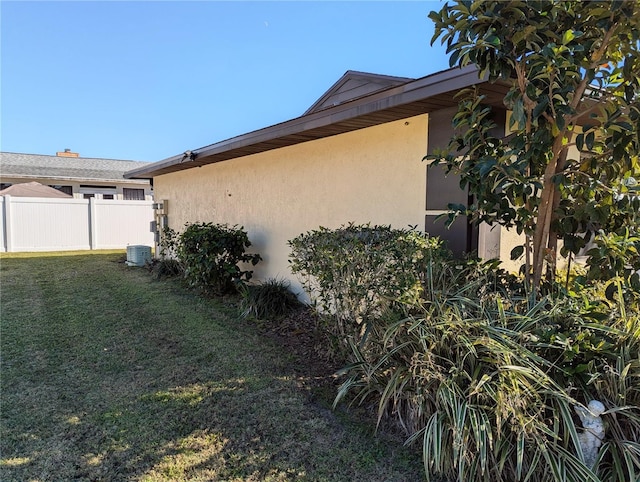 view of side of home featuring a lawn, fence, and stucco siding