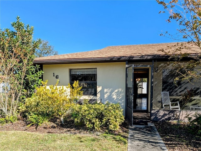 doorway to property featuring roof with shingles and stucco siding