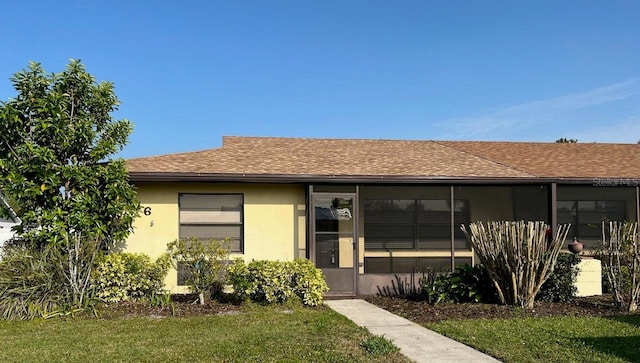 view of front of home with a shingled roof, a front yard, a sunroom, and stucco siding