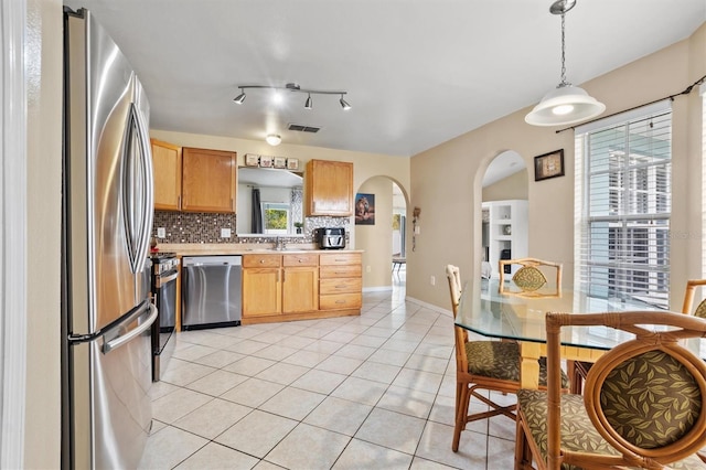 kitchen featuring backsplash, a healthy amount of sunlight, stainless steel appliances, and hanging light fixtures