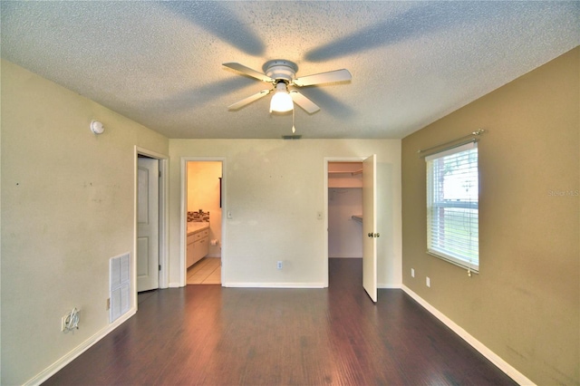 unfurnished bedroom featuring dark hardwood / wood-style flooring, ensuite bath, a textured ceiling, ceiling fan, and a spacious closet