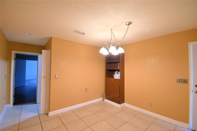 spare room featuring light tile patterned floors, a textured ceiling, and an inviting chandelier