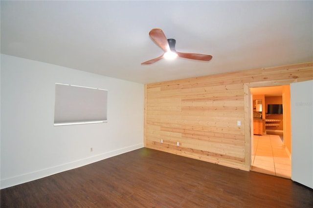 spare room featuring dark hardwood / wood-style floors, ceiling fan, and wooden walls