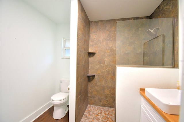 bathroom with a tile shower, vanity, toilet, and hardwood / wood-style floors