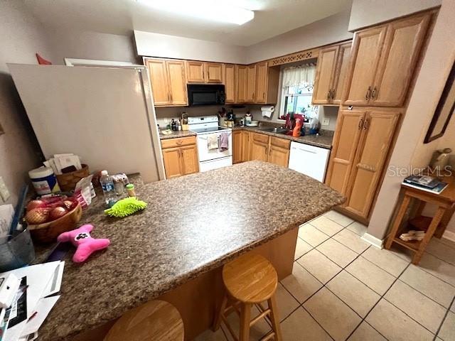 kitchen featuring kitchen peninsula, a kitchen breakfast bar, white appliances, and light tile patterned flooring