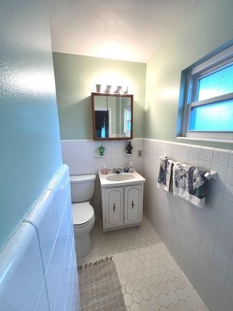 bathroom featuring tile patterned flooring, vanity, toilet, and tile walls