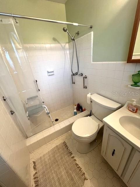 bathroom with vanity, tiled shower, tile walls, tile patterned flooring, and toilet