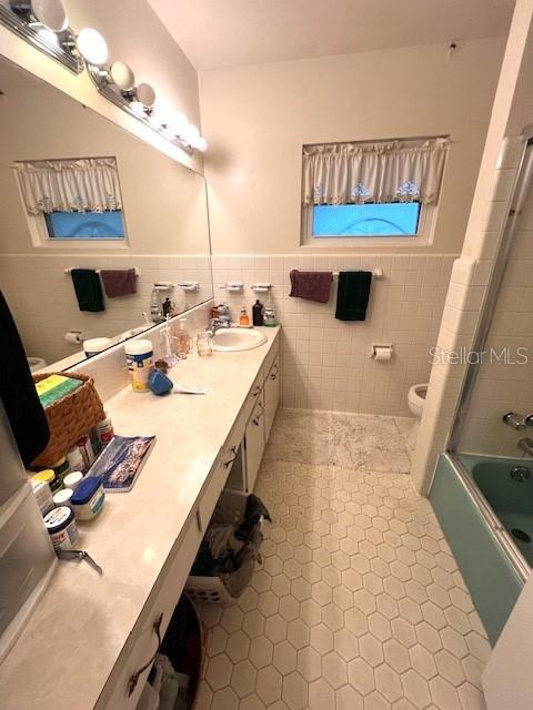 full bathroom featuring vanity, toilet, tile walls, and bath / shower combo with glass door