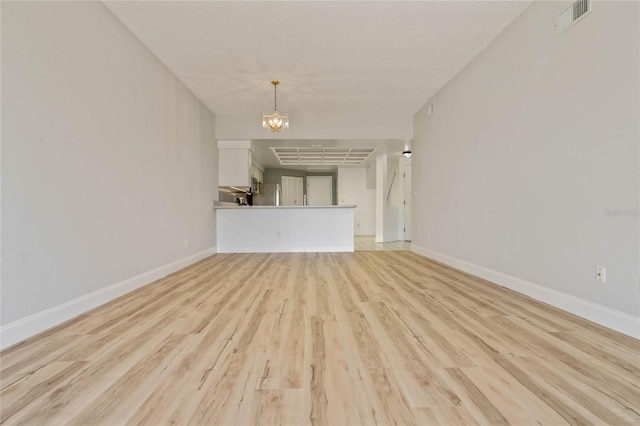 unfurnished living room featuring light wood-type flooring and an inviting chandelier