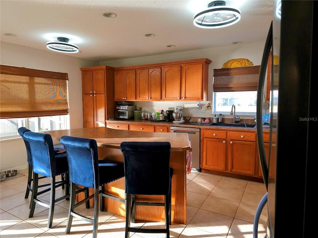 kitchen featuring a breakfast bar, black refrigerator, sink, stainless steel dishwasher, and light tile patterned floors