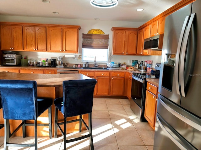 kitchen featuring a kitchen breakfast bar, sink, light tile patterned floors, and appliances with stainless steel finishes