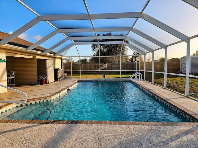 view of swimming pool with glass enclosure, a storage unit, and a patio area