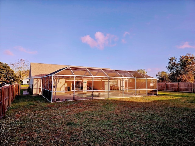 back house at dusk with a lawn and glass enclosure