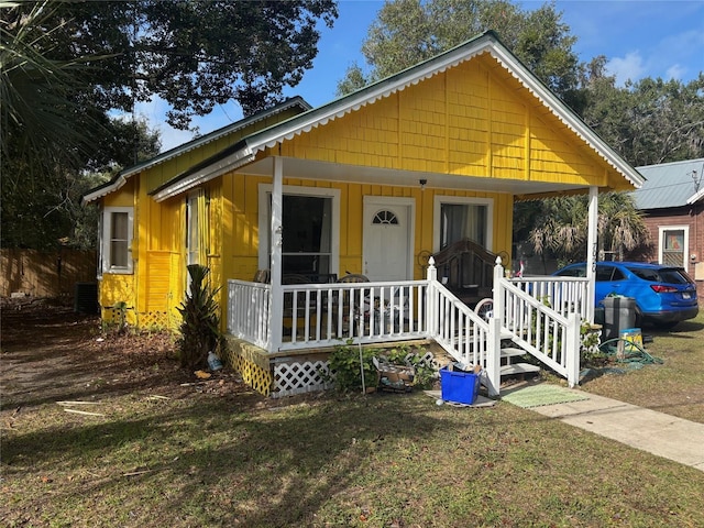 bungalow-style home with covered porch, a front lawn, and cooling unit