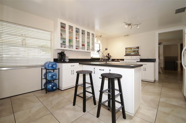 kitchen with a kitchen bar, white range, white cabinets, a kitchen island, and light tile patterned flooring