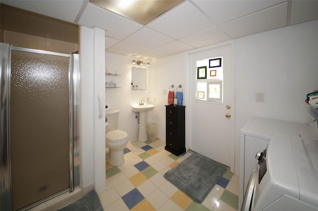 bathroom featuring washer and dryer, a drop ceiling, toilet, and a shower with door