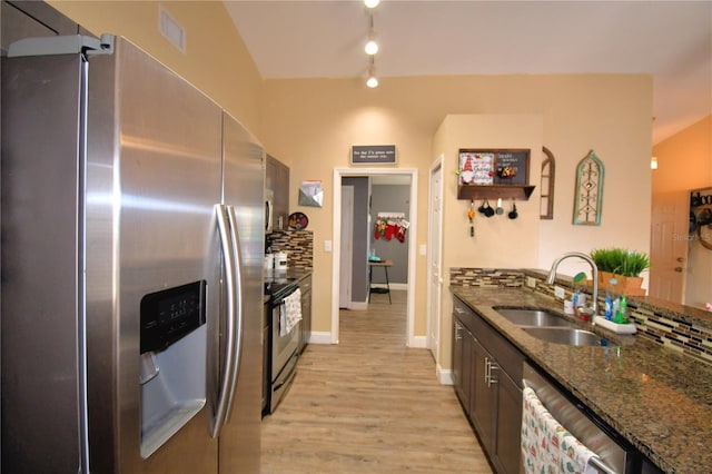 kitchen featuring backsplash, sink, light hardwood / wood-style flooring, dark stone countertops, and stainless steel appliances