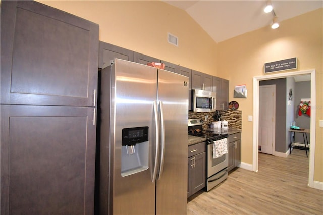 kitchen featuring light hardwood / wood-style floors, lofted ceiling, appliances with stainless steel finishes, and tasteful backsplash