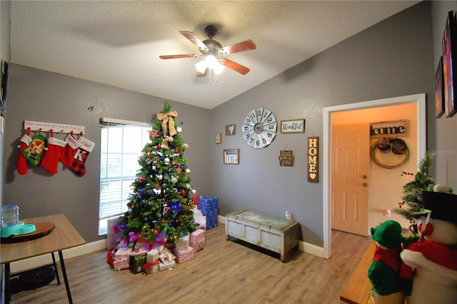 playroom with ceiling fan, lofted ceiling, a textured ceiling, and light hardwood / wood-style flooring