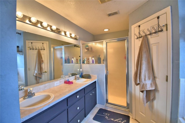 bathroom with tile patterned floors, vanity, a shower with shower door, and a textured ceiling