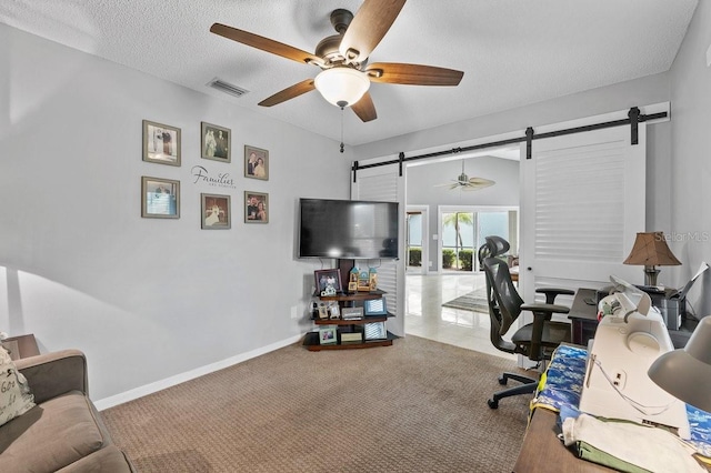 home office with a textured ceiling, a barn door, carpet floors, and ceiling fan