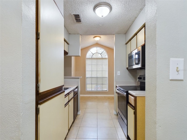 kitchen with lofted ceiling, light tile patterned floors, stainless steel appliances, and a textured ceiling