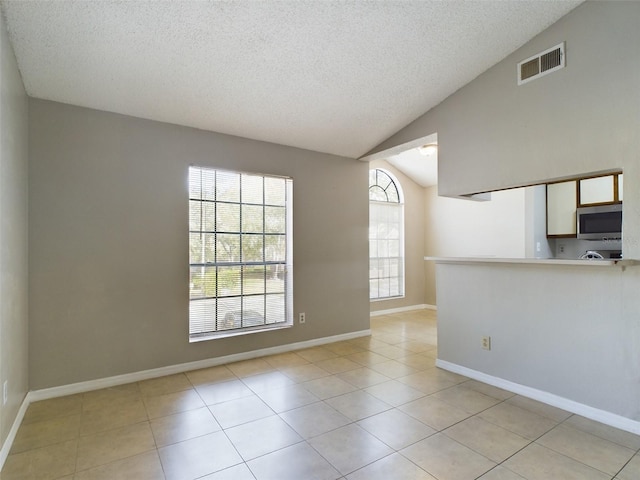 tiled empty room featuring a textured ceiling and lofted ceiling