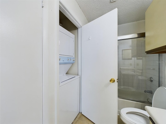 bathroom with enclosed tub / shower combo, tile patterned floors, a textured ceiling, toilet, and stacked washer and clothes dryer