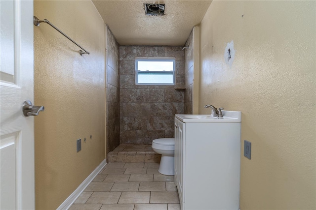 bathroom with tile patterned floors, a tile shower, a textured ceiling, vanity, and toilet