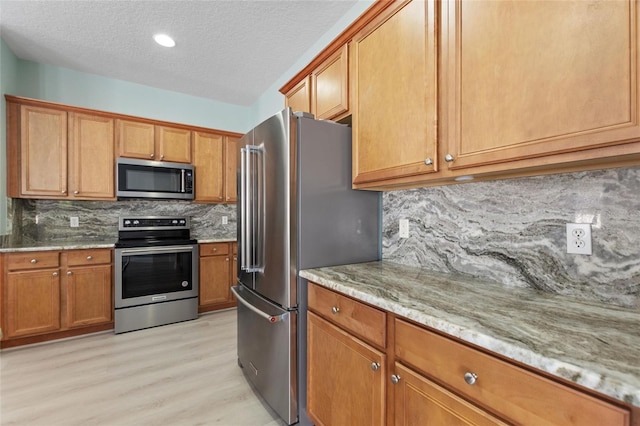 kitchen with light stone counters, backsplash, a textured ceiling, appliances with stainless steel finishes, and light wood-type flooring