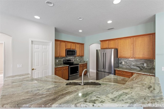 kitchen featuring sink, stainless steel appliances, light stone counters, kitchen peninsula, and decorative backsplash