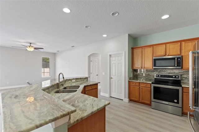 kitchen featuring a center island with sink, sink, decorative backsplash, ceiling fan, and stainless steel appliances