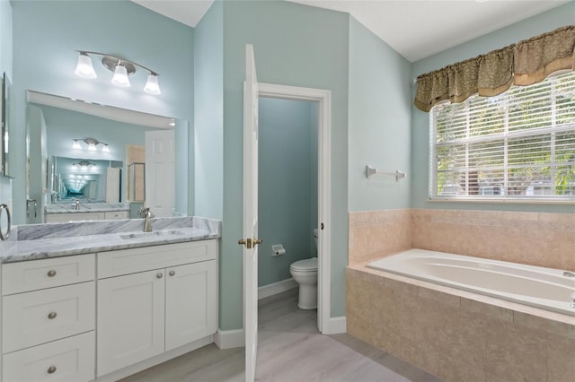 bathroom with vanity, toilet, and tiled bath